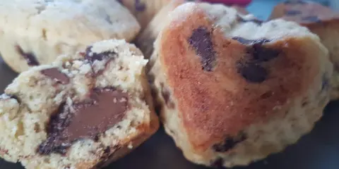 Gros plan sur des cookies moelleux en forme de cœur, débordant de pépites de chocolat. Un cookie est coupé en deux, révélant un cœur fondant.