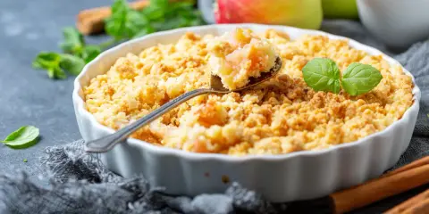 Une cuillère prélève une bouchée dorée de ce meilleur crumble aux pommes, garni de feuilles de menthe fraîche.