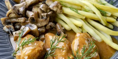Pyszne medaliony z indyka w sosie, podane z duszonymi pieczarkami i żółtą fasolką szparagową.