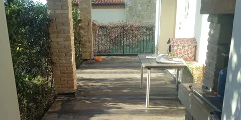Terrazzo con pavimentazione scura, ideale per l'impermeabilizzazione. Tavolo, barbecue e vegetazione completano la scena.