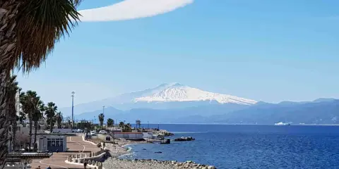 Lungomare di Reggio Calabria con vista sull'Etna innevato. Perfetto per scoprire cosa visitare a Reggio Calabria, tra palme e mare blu.