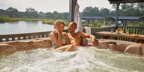 A happy couple enjoys a hot tub with a view of a serene gay lake.