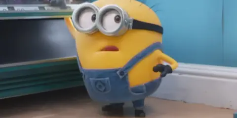Minionek w ogrodniczkach zastanawia się, po jakim języku mówią minionki, gdy patrzy na automat z przekąskami.
