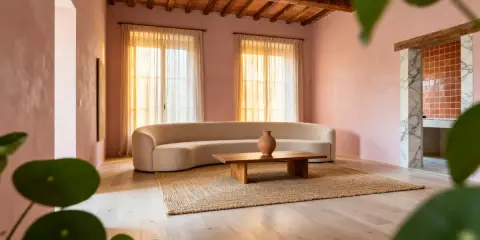 Salon aux murs roses, canapé courbe, table basse en bois et tapis en jute. Une ambiance douce et harmonieuse pour une maison feng shui.