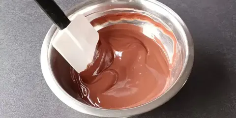 Spatule mélangeant une ganache au chocolat noir onctueuse dans un bol en métal.