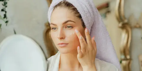 Kobieta z ręcznikiem na głowie aplikuje krem na twarz, przygotowując się do swojego codziennego glow up.