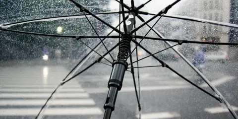 Przezroczysty parasol w deszczu, z widocznym stelażem i kroplami wody. Zastanawiasz się, czy można zabrać parasol do samolotu?