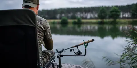 Wędkarz w kamuflażu czeka nad jeziorem. Czy to odpowiednia wędka do metody?