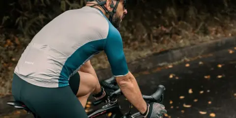 Ciclista con casco e occhiali pedala su strada bagnata, godendosi l'aria fresca. Un modo perfetto per alternare bici e camminata.