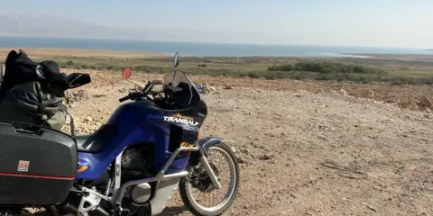 Motocykl Honda Transalp z bagażami gotowy do podróży, z widokiem na Morze Martwe. Dokumenty, jak **carnet de passage**, czekają na przygodę.