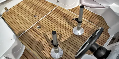 Pont de bateau avec un revêtement imitation teck, deux supports de table et un volant.