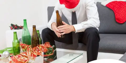 Smutny mężczyzna w czapce Mikołaja siedzi z butelką piwa, otoczony pustymi butelkami. Szukasz co zamiast alkoholu?