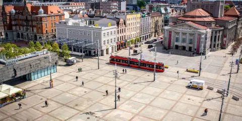 Rynek w Katowicach z czerwonym tramwajem i ludźmi spacerującymi po placu. Idealne miejsce na odkrywanie katowickich atrakcji dla młodzieży.
