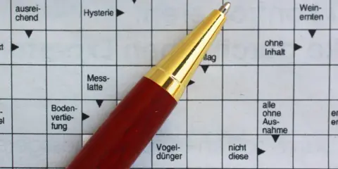 Ein roter Stift liegt auf einem Kreuzworträtsel mit deutschen Begriffen.