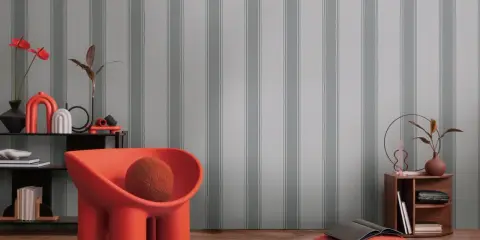 Pomarańczowe krzesło i dekoracje na tle tapety w szare pasy.