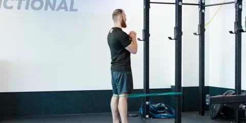 Mężczyzna wykonuje ćwiczenie spanish squat z gumą oporową wokół ud, przygotowując się do przysiadu.