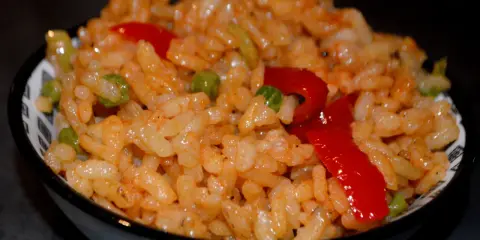 Un bol de riz coloré avec des petits pois et des poivrons rouges, parfait pour une recette salade riz facile et rapide.