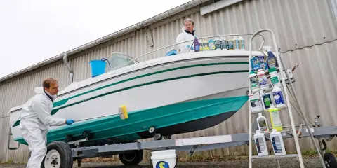 Un homme en combinaison blanche nettoie le flanc d'un bateau blanc et vert sur une remorque. Le nettoyage du pont du bateau est en cours.