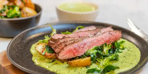 Saftig flankstek ugn serveras med rostade potatisar, grönsaker och en krämig örtsås. En festlig måltid!