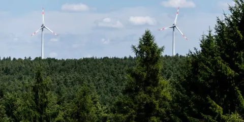 Zwei Windräder ragen über einen dichten Wald. Ein Onshore-Windpark in Deutschland, der saubere Energie erzeugt.