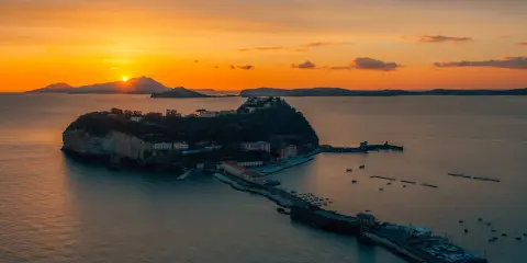 Tramonto infuocato sul golfo di Napoli, con una suggestiva isoletta che emerge dal mare calmo, illuminata dagli ultimi raggi dorati.