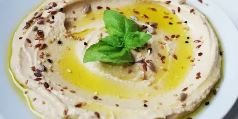 Cremiger Hummus, garniert mit Öl, Kräutern und Samen. Tahin ist die geheime Zutat für diese köstliche Dip-Kreation.