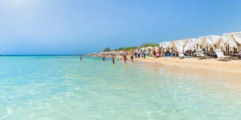 Spiaggia pugliese con acque cristalline e lettini sotto gazebo bianchi, ideale località mare Puglia per famiglie.
