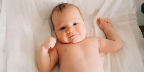 Uśmiechnięte niemowlę leży na białym tle, ćwicząc mięśnie. Wygląda, jakby zaraz miało stanąć na głowie.