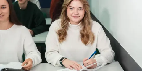 Uśmiechnięta studentka pisze w zeszycie, idealne zdjęcie do legitymacji.