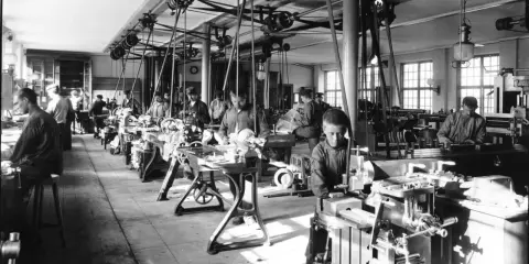 Barn arbetar vid maskiner i en verkstad, en scen från den industriella revolutionen.