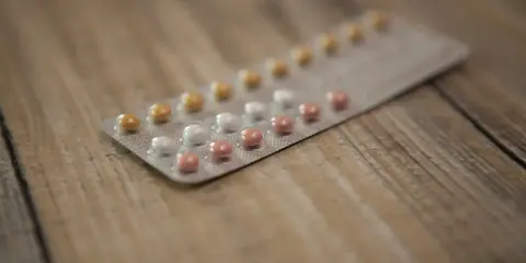 Opakowanie tabletek antykoncepcyjnych z różowymi, białymi i żółtymi pigułkami na drewnianym tle.