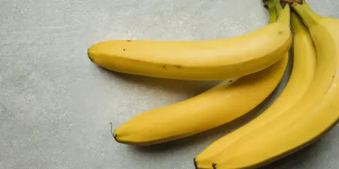 Kilka żółtych bananów leżących na szarym tle.