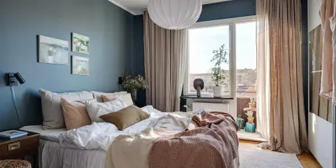 Accogliente camera da letto blu e beige con letto comodo, quadri astratti e grande finestra luminosa.