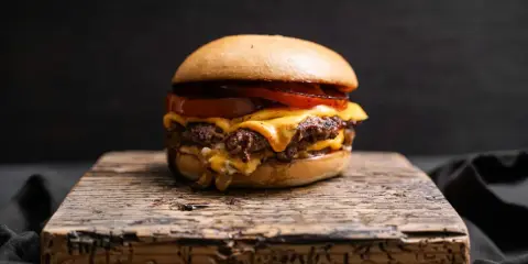 Saftiger Oklahoma Smash Burger mit geschmolzenem Käse und Tomaten auf rustikalem Holzbrett.