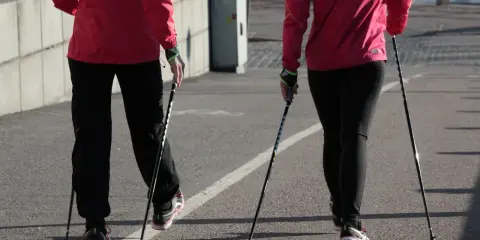 Dwie osoby w czerwonych kurtkach i czarnych spodniach maszerują z kijki do nordic walking.