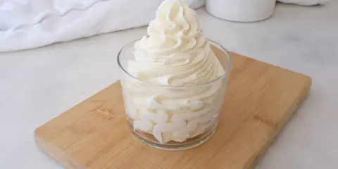 Crème au beurre sucre glace, onctueuse et aérienne, dressée dans un verre sur une planche en bois.