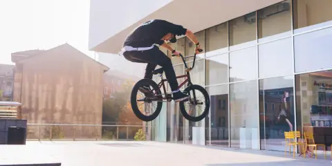 Chłopak na BMX-ie wykonuje bunny hop, unosząc rower w powietrze przed nowoczesnym budynkiem.