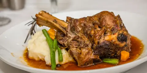 Une souris d'agneau braisée, servie avec une purée onctueuse, des haricots verts croquants et des dés de carottes, le tout nappé d'une sauce savoureuse.