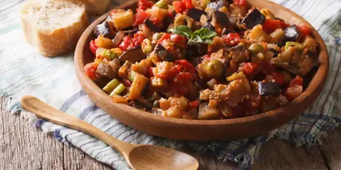 Un plat de caponata, une recette sicilienne savoureuse, garni de basilic frais, servi avec du pain croustillant.