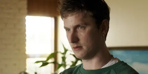 Mikkel Boe Følsgaard, en ung man med grönt linne, tittar bort. Bakom honom syns en växt och ett fönster.