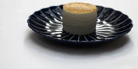 Un cylindre blanc, saupoudré d'or, sur une assiette bleue. Une idée de quoi manger à Paris pour une expérience culinaire unique.