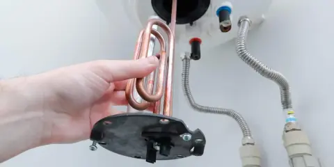 Mano retirando resistencia de cobre para saber como limpiar un termo por dentro.