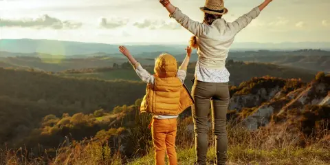 Bambini in Toscana, con le braccia al cielo, ammirano un paesaggio collinare al tramonto.