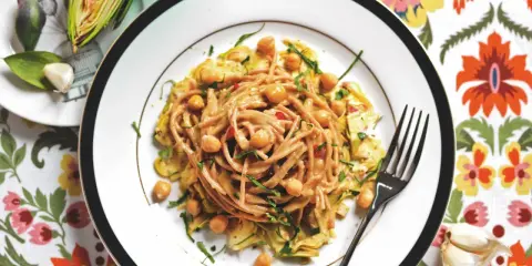 Un piatto invitante di pasta con carciofi alla siciliana, arricchito da ceci e erbe fresche, su un tovagliolo colorato.