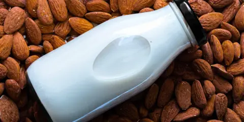 Bouteille de lait d'amande maison posée sur un lit d'amandes entières.