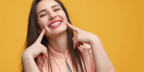 Une jeune femme au sourire éclatant, doigts pointés vers ses joues, semble expliquer la signification d'un sourire pincé.