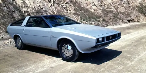 Srebrny Hyundai Pony z lat 70. na drodze w skalistym terenie.