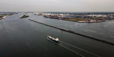 Una nave solca le acque di quello che è il più grande porto d'Europa, con industrie e serbatoi sullo sfondo.