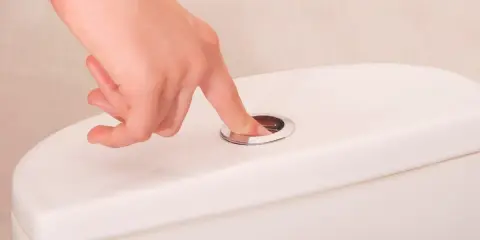 Main tenant appuie sur le bouton de la chasse d'eau, mais elle ne se remplit pas. Problème de plomberie à résoudre.