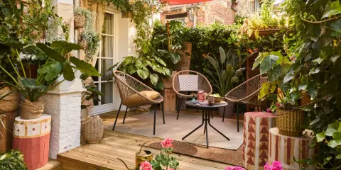 Aménager une petite terrasse sans se ruiner : trois fauteuils en rotin, une table basse, des plantes luxuriantes et une toile rouge créent un coin cosy et abordable.